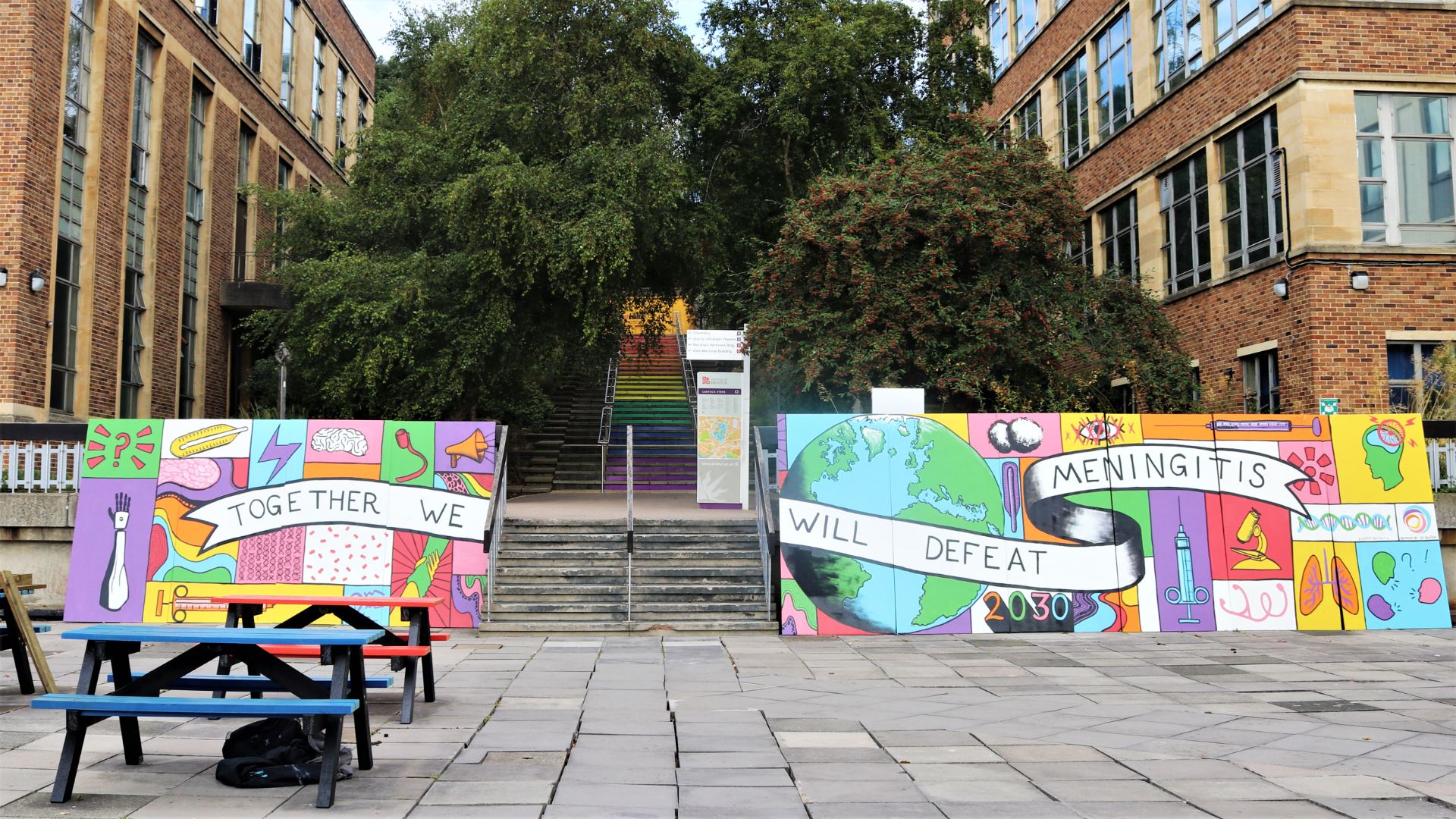Temporary mural on boards situated at bottom of steps saying Together we will defeat meningitis